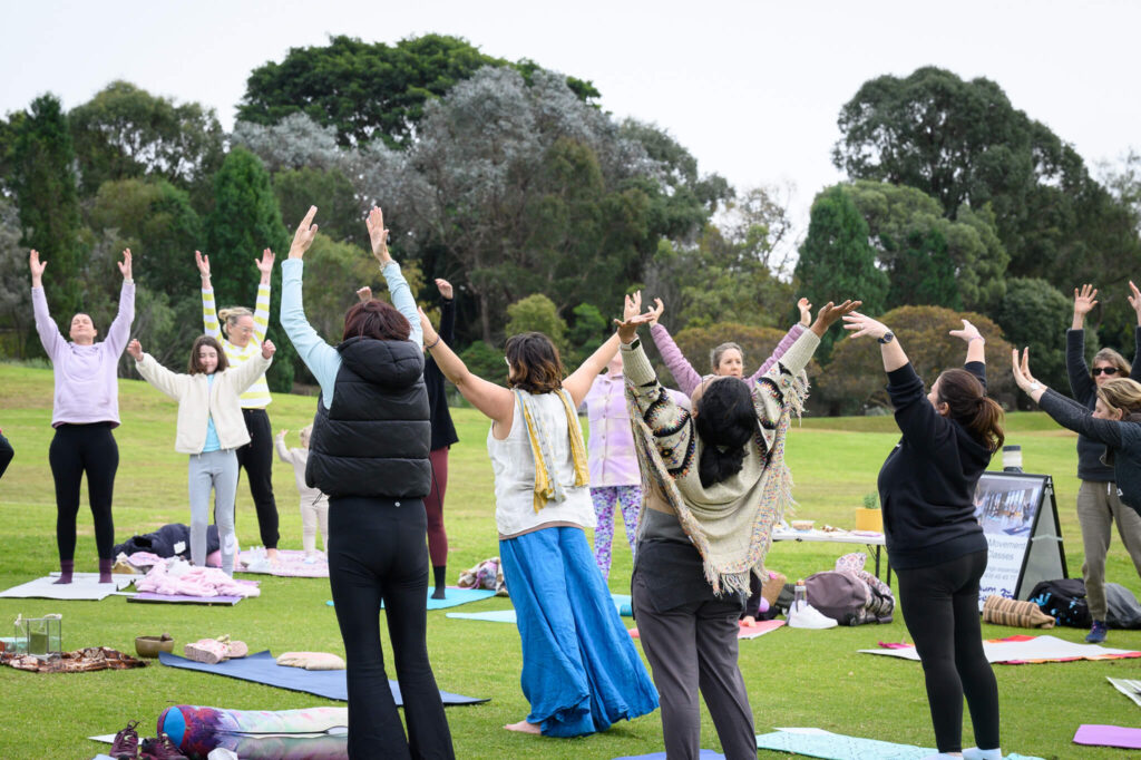 Group of ladies doing yoga outdoors with arms up and open to receive breath